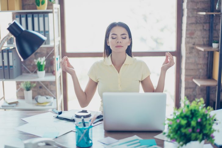 Female office worker meditating at her desk to reduce stress